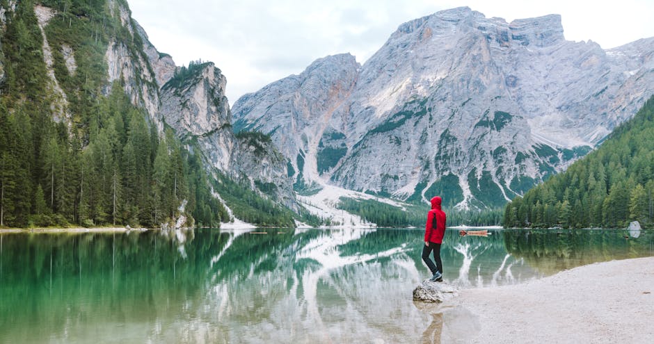 Person standing by the scenic Lake Braies with majestic Dolomite mountains reflected in the water.